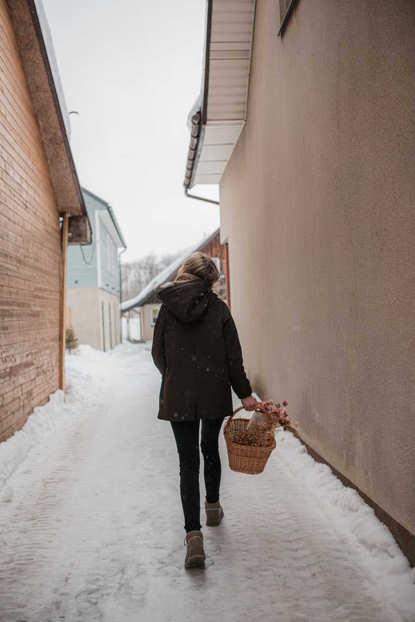 Moteris su ruda gėlėta sodo striuke žiemos mieste — eina su gėlių krepšeliu