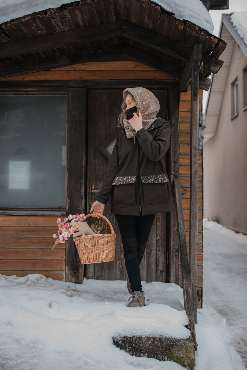 Moteris su ruda gėlėta sodo striuke žiemą — kalba telefonu ir laiko gėlių krepšelį